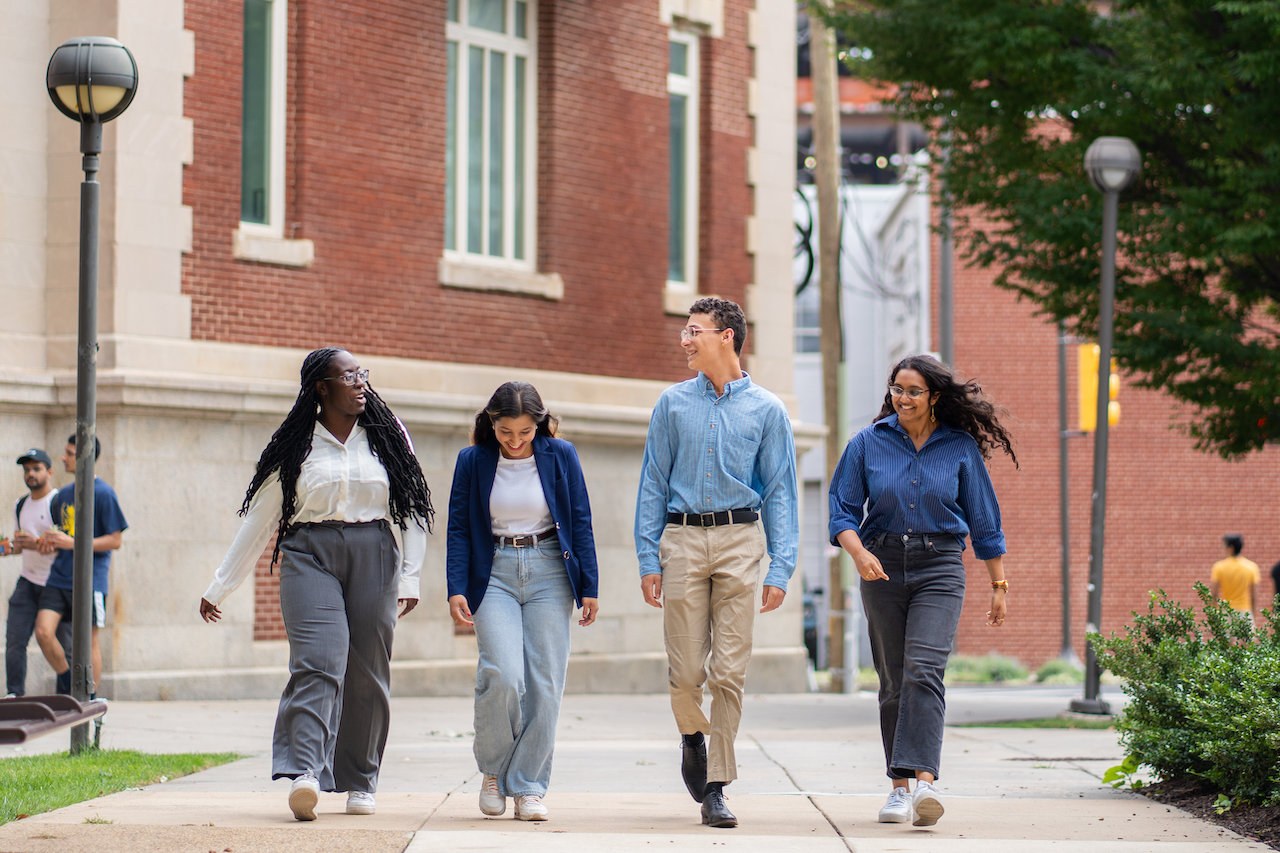 Four students walking on campus behind the Drexel Dornsife School of Public Health 